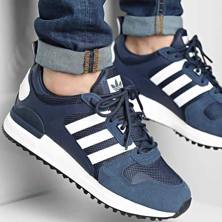Le modèle présenté dans l'image est la adidas ZX 700 HD dans son coloris bleu marine classique avec les trois bandes blanches caractéristiques de la marque adidas.