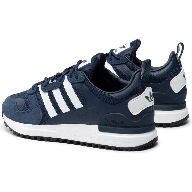 Le modèle présenté dans l'image est la adidas ZX 700 HD dans son coloris bleu marine classique avec les trois bandes blanches caractéristiques de la marque adidas.