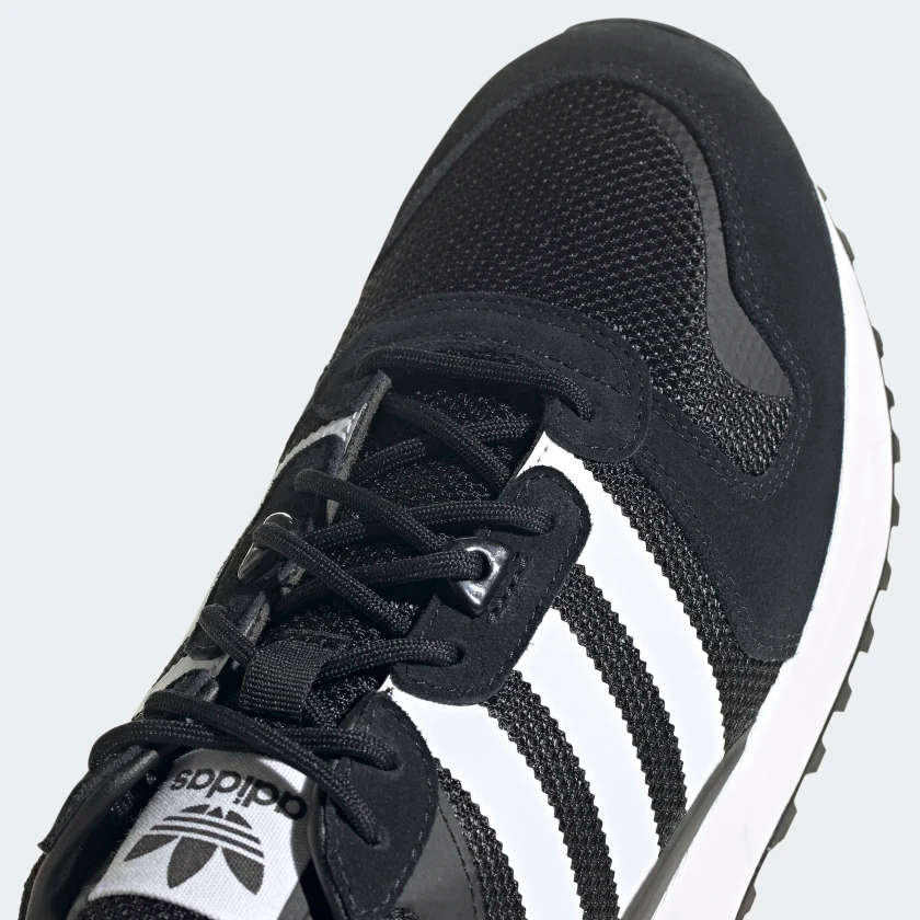 Le modèle présenté dans l'image est la adidas ZX 700 HD dans son coloris bleu marine classique avec les trois bandes blanches caractéristiques de la marque adidas.