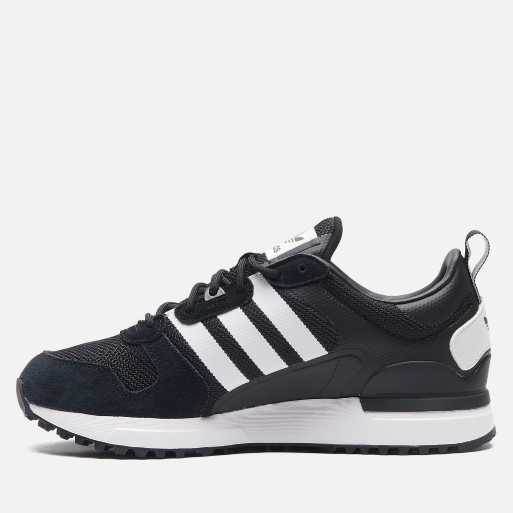 Le modèle présenté dans l'image est la adidas ZX 700 HD dans son coloris bleu marine classique avec les trois bandes blanches caractéristiques de la marque adidas.