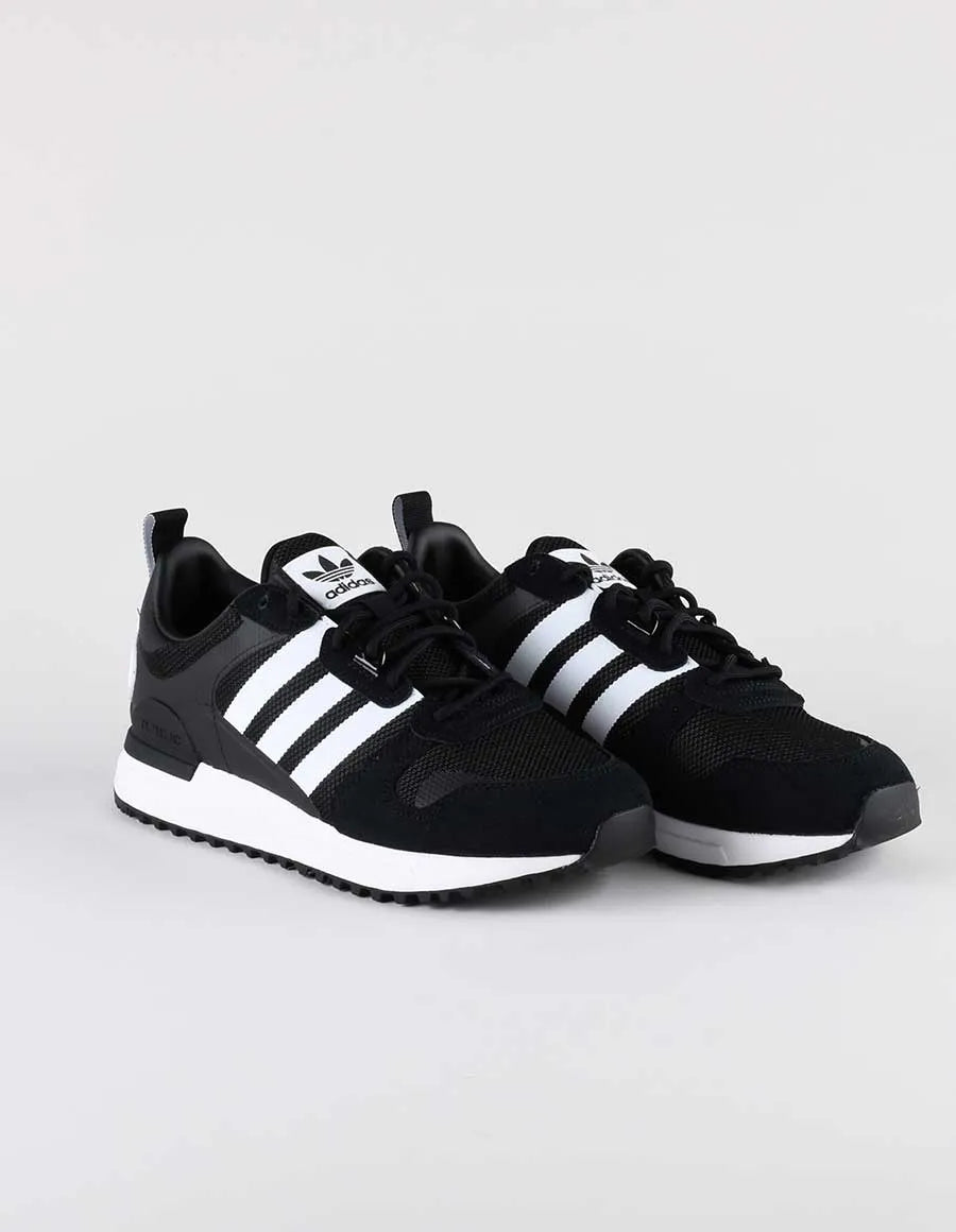 Le modèle présenté dans l'image est la adidas ZX 700 HD dans son coloris bleu marine classique avec les trois bandes blanches caractéristiques de la marque adidas.