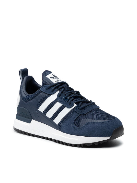 Le modèle présenté dans l'image est la adidas ZX 700 HD dans son coloris bleu marine classique avec les trois bandes blanches caractéristiques de la marque adidas.