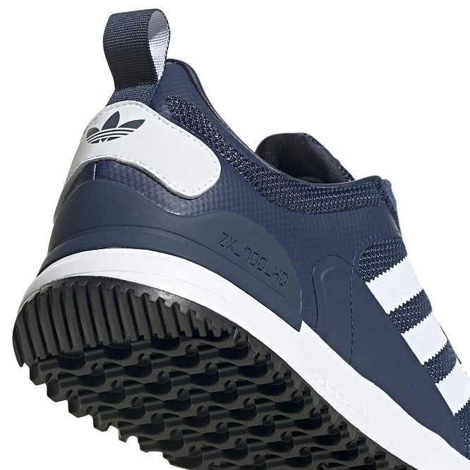 Le modèle présenté dans l'image est la adidas ZX 700 HD dans son coloris bleu marine classique avec les trois bandes blanches caractéristiques de la marque adidas.