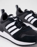 Le modèle présenté dans l'image est la adidas ZX 700 HD dans son coloris bleu marine classique avec les trois bandes blanches caractéristiques de la marque adidas.