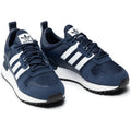 Le modèle présenté dans l'image est la adidas ZX 700 HD dans son coloris bleu marine classique avec les trois bandes blanches caractéristiques de la marque adidas.
